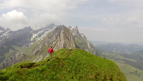 A-man-in-a-red-jacket-is-walking-on-top-of-a-mountain-and-is-followed-by-the-drone