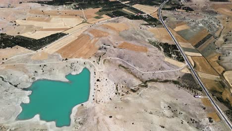 Drone-filming-of-a-small-lake-lost-between-hills-and-fields-near-a-road-in-Turkey