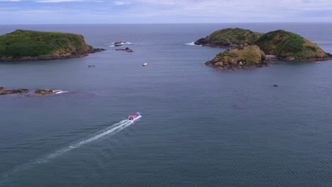 Aerial-seascape-of-a-boat-traveling-around-the-costal-island-on-the-coast-of-Punihuil,-Chiloe-Island,-bright-sunny-day
