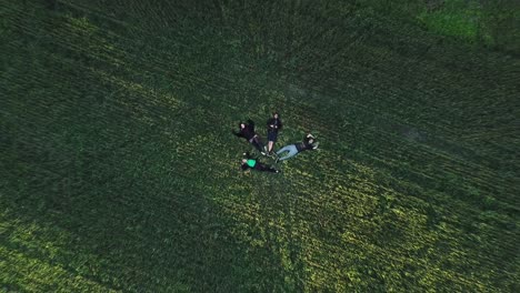 Group-Of-Friends-Lying-On-The-Grassy-Ground-Near-Windmill---top-down-drone-shot