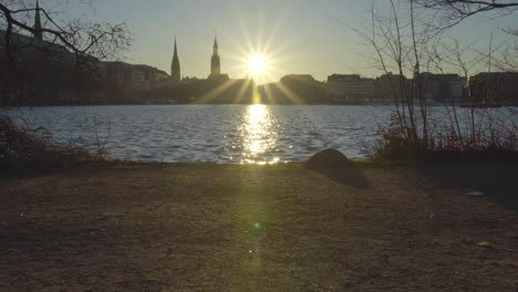 View-of-the-sun-setting-on-Hamburg,-Germany,-in-Dec-2019-across-Inner-Alster-Lake-with-people-walking