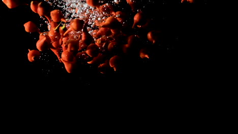 Beak-peppers-dropped-into-water-on-black-background,-slow-motion-close-up