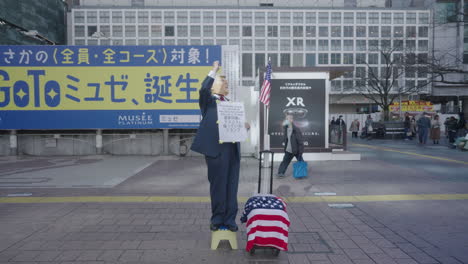 Hombre-Vestido-Como-Donald-Trump-Mostrando-Apoyo-Sosteniendo-Un-Cartel-En-El-Cruce-De-Shibuya-Durante-Una-Pandemia-En-Tokio,-Japón