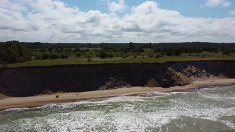 Flying-Over-Coastline-Baltic-Sea-Ulmale-Seashore-Bluffs-Near-Pavilosta-Latvia-and-Landslides-With-an-Overgrown,-Rippling-Cave-Dotted-Cliff-and-Pebbles