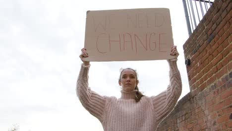 Strong-woman-standing-in-protest-holding-a-sign-for-change-on-a-street-low-angle