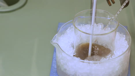 Stirring-Chemical-Solution-In-A-Beaker-While-Cooling-In-Ice-With-Thermometer---tilt-down-shot
