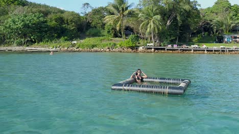 Model-sitting-and-waving-in-a-floating-device-in-the-ocean,-Koh-Kood,-Thailand