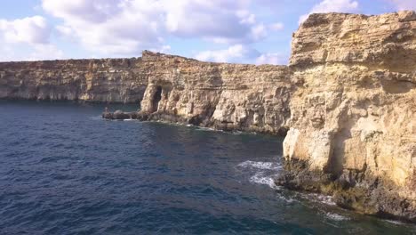 Low-angle-view-of-sheer-limestone-cliffs-battered-by-the-waves-of-the-Mediterranean-Sea-off-the-coast-of-Malta