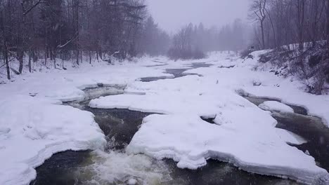 SLOW-MOTION-shot-of-icy-river-with-small-waterfall-during-snow-storm
