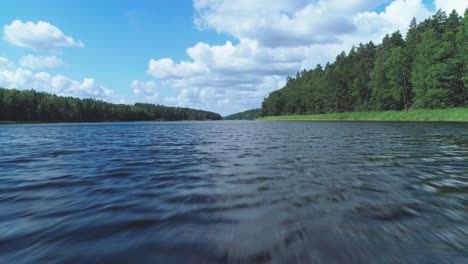 Luftaufnahme-über-Einem-Dunkelblauen-Fluss-In-Schweden-Bei-Tag,-Umgeben-Von-Grünem-Wald-Und-Einem-Blauen-Himmel-Mit-Vereinzelten-Wolken