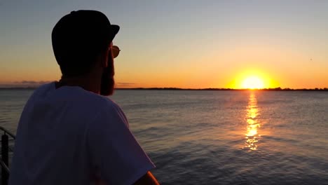 Bearded-Man-with-Rounded-Sun-Glasses-Staring-at-the-Sunset-on-a-Deck