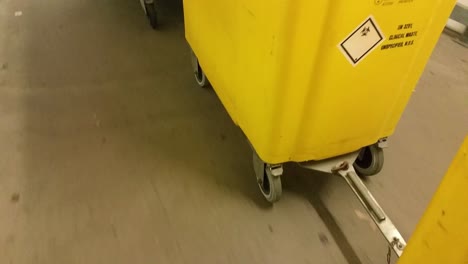 Yellow-medical-waste-bins-wheeled-down-corridor