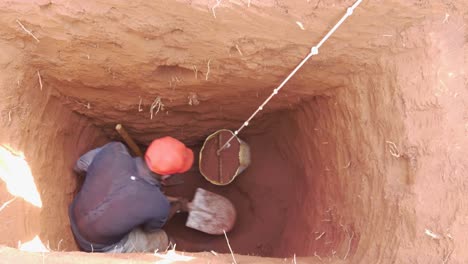An-African-man-inside-a-deep-hole-being-dug-out-into-a-pit-latrine-loading-soil-into-a-bucket-to-be-carted-out