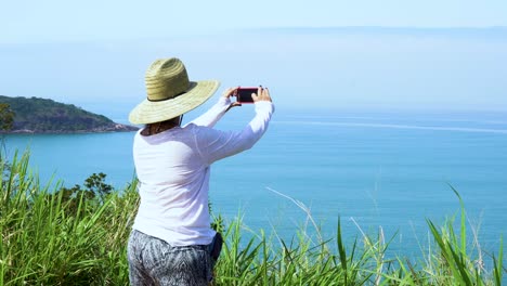 woman-wearing-hat-taking-pictures-of-beach