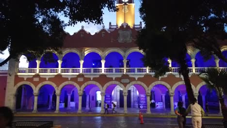 Pushing-in-to-the-Municipal-building-at-dusk-with-its-blue-lights-next-to-the-plaza-grande-in-Merida,-Mexico