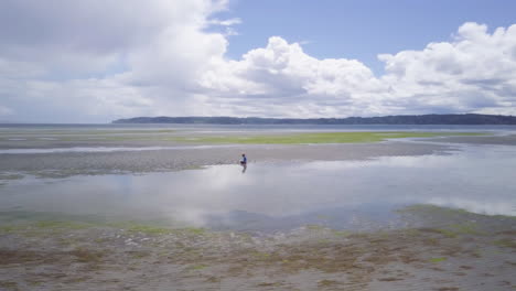 Wide-aerial-of-boy-playing-in-sand-on-beach-at-low-tide