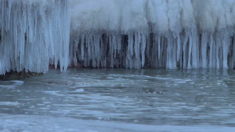 Kleine-Wellen-Brechen-An-Einem-Bewölkten-Wintertag-Gegen-Die-Ruinen-Der-Nördlichen-Festungsanlage-Karosta-Am-Ufer-Der-Ostsee,-Bedeckt-Mit-Eis,-Schnee-Und-Eiszapfen,-Nahaufnahme