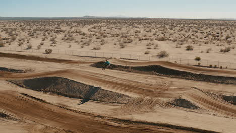 Aerial-Tracking-Pan,-Motocross-rider-jumping-and-catching-air-on-desert-circuit
