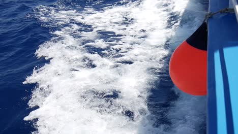 View-looking-down-the-side-of-a-speeding-boat-at-the-waves-and-wake-in-the-water-as-a-red-buoy-hangs-over-the-edge-of-the-boat