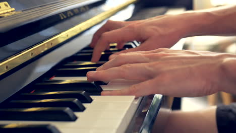 A-close-up-of-a-man-playing-a-black-piano-with-his-hands-and-fingers-in-the-light-of-a-window
