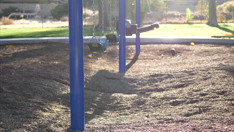 Slide-left-through-a-sunny-kids-park-playground-with-an-empty-blue-swing-set