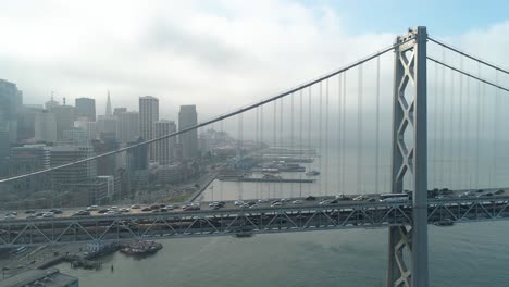 Luftaufnahme-Von-Fahrzeugen,-Die-Sich-Auf-Der-San-Francisco-oakland-Bay-Bridge-Mit-Der-Stadt-Im-Hintergrund-Bewegen