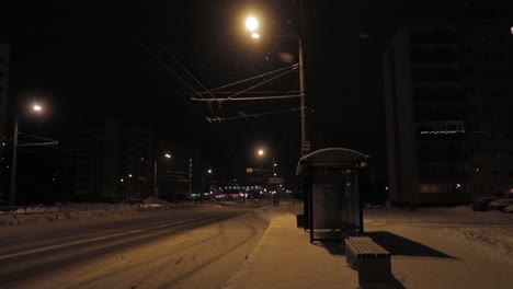 Bushaltestelle-Bei-Nacht-In-Schneebedeckter-Straße-Und-Schneefall-Mit-Warmen-Lichtern,-Die-Die-Straße-Erhellen