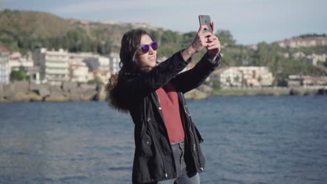 Wide-shot-of-a-girl-taking-selfie-and-pictures-with-sea-in-the-background-in-slow-motion