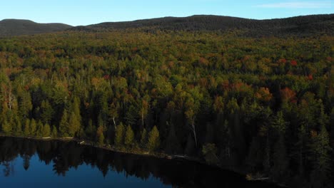 Aerial-drone-shot-over-the-edge-of-a-mountain-lake-with-colorful-autumn-trees-along-the-shore-as-summer-ends-and-the-season-changes-to-fall-in-Maine