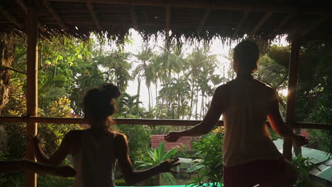 Pulling-back-over-the-shoulders-of-a-group-of-travelers-enjoying-a-sunset-meditation-and-yoga-session-on-a-sunny-wooden-porch-overlooking-the-rainforest-and-jungle-leading-out-to-the-beach