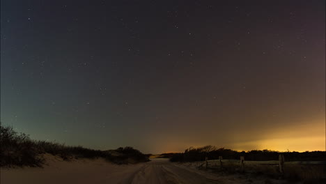 A-beautiful-starry-night-sky-rotates-above-a-dirt-road-at-the-beach-surrounded-by-dunes