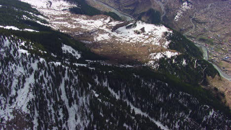 Luftaufnahme-über-Das-Tal-Mit-Bunten-Häusern,-Lebensstil-Und-Fluss-Mit-Malerischem-Blick-Auf-Berge,-Deren-Gipfel-Mit-Schnee-Und-Kiefernwald-Bedeckt-Sind