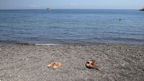 A-pair-of-leather-beach-sandals-on-a-black-peddle-beach-in-Santorini,-called-Kamari
