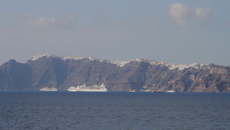 A-view-of-the-majestic-black-cliffs-of-Santorini-with-a-village-built-on-the-edge-of-them,-cruise-ships-parked-just-below