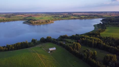Aerial-shot-of-a-secluded-lake,-surrounded-by-fields-and-farms