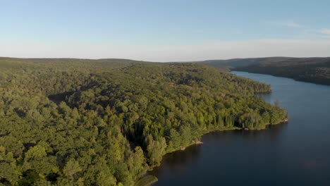 Langsame-Luftaufnahme-Des-Sees-In-Quebec,-Umgeben-Von-Bäumen-Bei-Sonnenaufgang,-Wenn-Die-Sonne-über-Den-Hügel-Und-Die-Bäume-Scheint