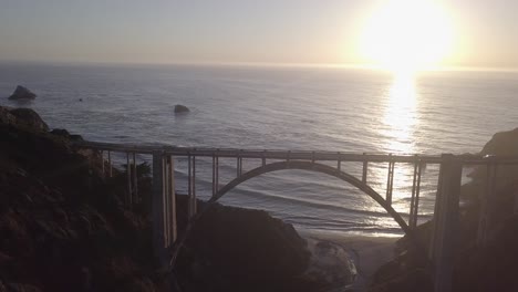 Aerial-Drone-Shot-of-Bixby-Bridge-with-Sun-and-Ocean-Behind
