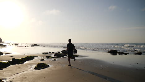 Ein-Starker-Mann-Im-Silhouettenlauf-Und-Fitnesstraining-Am-Strand-Bei-Sonnenaufgang-In-Santa-Barbara,-Kalifornien,-Zeitlupe