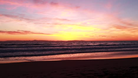Möwen-Fliegen-Am-Strand-Während-Eines-Wunderschönen-Sonnenuntergangs-In-Gelb,-Orange,-Rosa-Und-Blau-Mit-Dem-Huntington-Beach-Pier-Im-Hintergrund-In-Surf-City,-USA,-Kalifornien