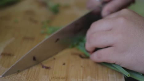 Closeup-on-a-woman-chopping-spring-onions-on-a-wooden-kitchen-table