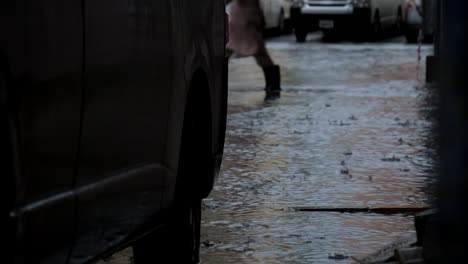 Man-walking-through-the-flooded-street-with-knee-high-boots-in-a-city-with-submerged-cars-parked-nearby-in-Al-Nahda,-Sharjah,-United-Arab-Emirates-after-a-heavy-rain-on-November-26,-2018