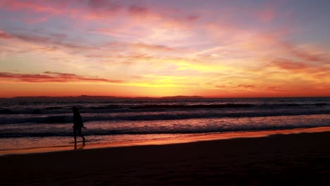 A-enjoys-her-vacation-at-the-beach-during-a-gorgeous-yellow,-orange,-pink-and-blue-sunset-with-the-Huntington-Beach-Pier-in-the-background-at-Surf-City-USA-California