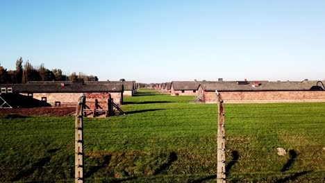 Drone-rising-behind-fence-and-pull-back-shot-of-the-barracks-in-Auswitz-Birkenau,-Poland,-Europe