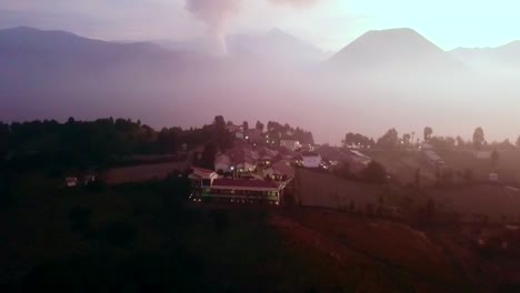 Drone-flying-over-a-resort-at-Bromo-volcano-at-dusk,-with-smoke-from-the-volcano