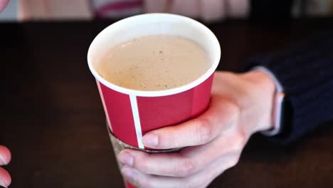 In-Einem-Café-Aufgenommener-Clip-Einer-Kaukasischen-Frau,-Die-Eine-Nachfüllbare-Tasse-Mit-Heißem-Kaffee-Oder-Tee-Darin-Trinkt-Und-Mit-Ihren-Händen-Spricht
