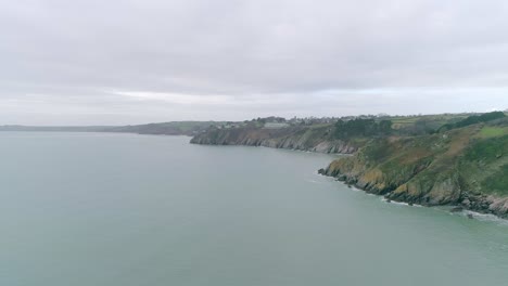 Top-down-aerial-tilt-up-to-reveal-a-kayaker-below-and-the-vast-challenging-coastline-beyond-them-looking-towards-the-ongoing-horizon