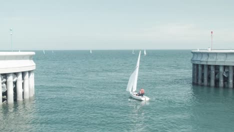 Sail-boat-with-sails-up-passes-through-harbor-making-way-to-the-sea