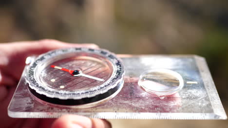 Close-up-on-a-compass-in-the-hands-of-a-lost-hiker-being-used-in-an-emergency-survival-situation-to-find-the-trail-and-location