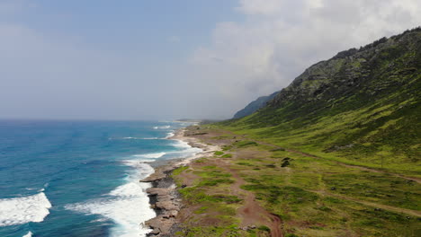Aerial-time-lapse-of-beautiful-ocean-waves-crashing-on-Hawaii-shoreline-with-green-mountain-cliffs-in-the-background