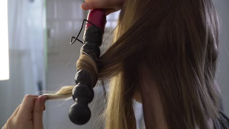 Blonde-haired-girl-curling-her-hair,-getting-ready-for-the-evening